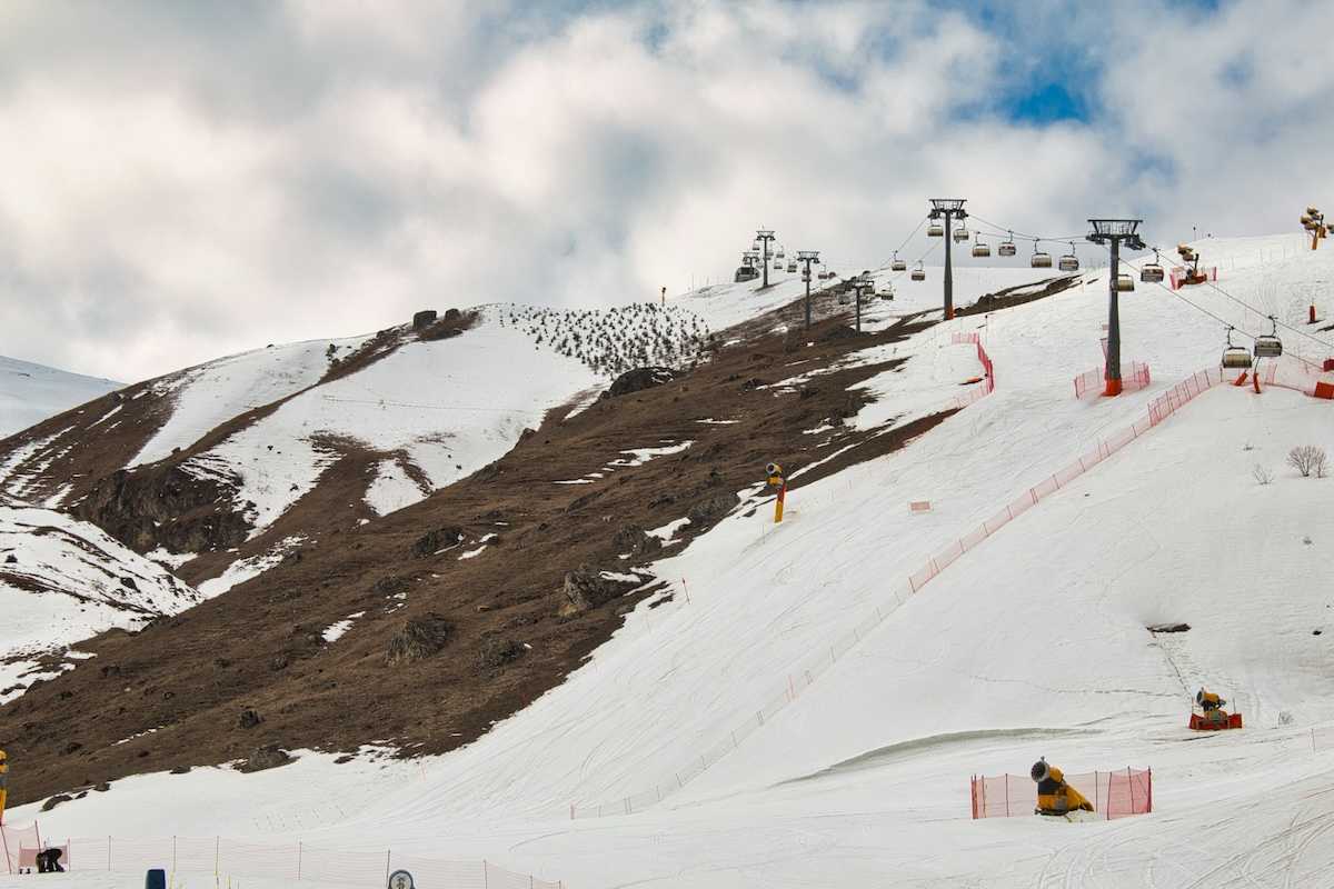 Ski lift on a partially snowy mountain with snowmaking equipment