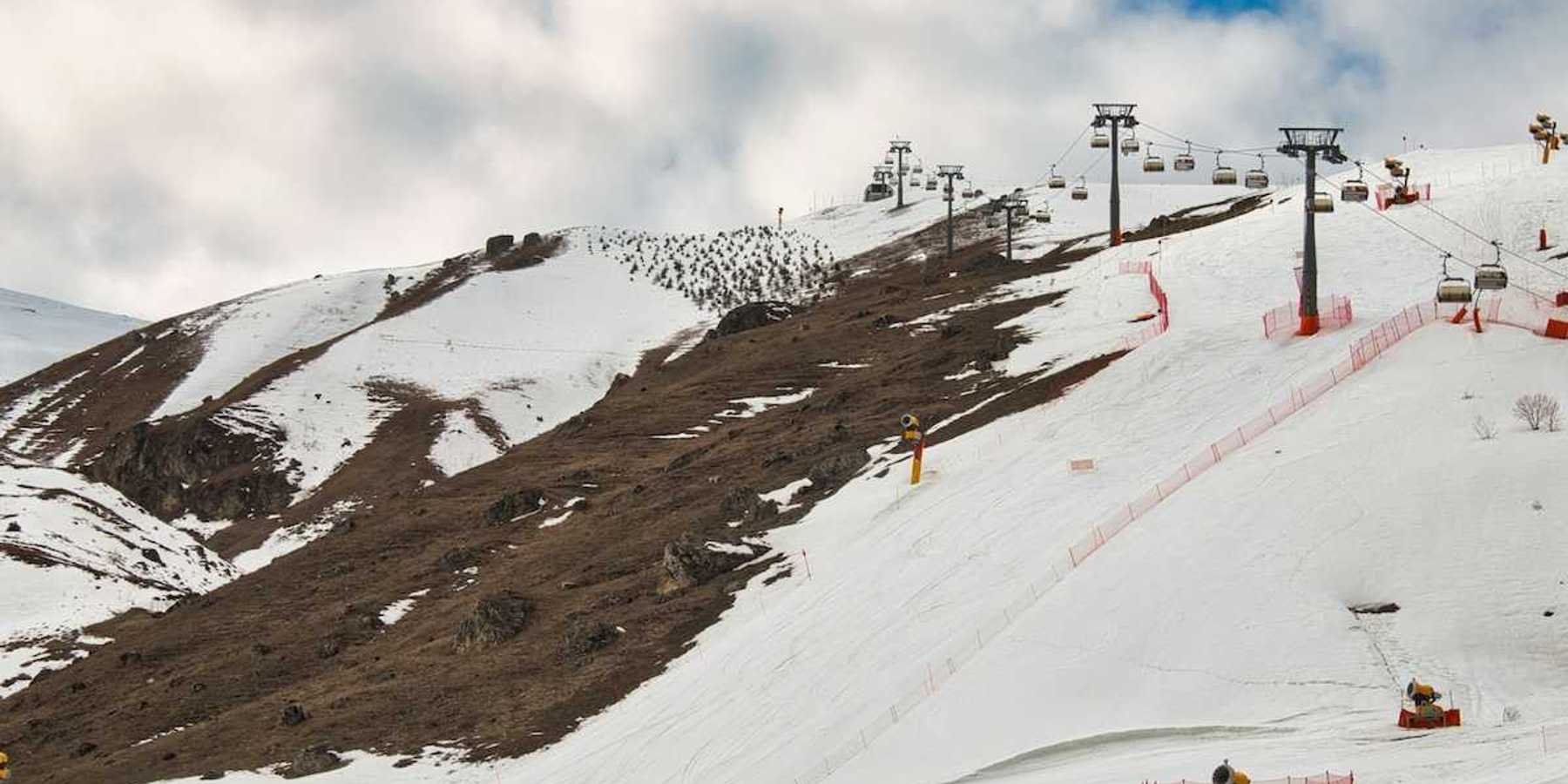Ski lift on a partially snowy mountain with snowmaking equipment