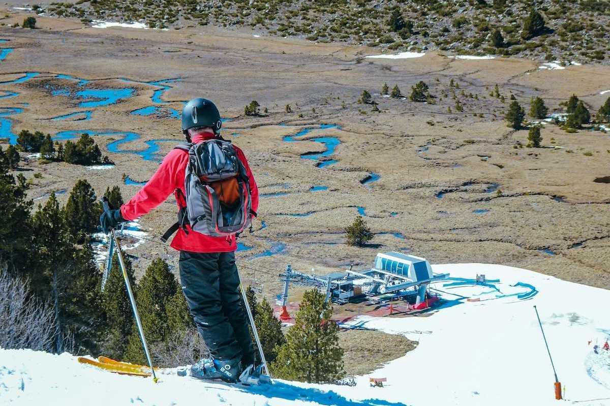 Skier in red jacket poised to descend to lift station. Spotty snow cover.