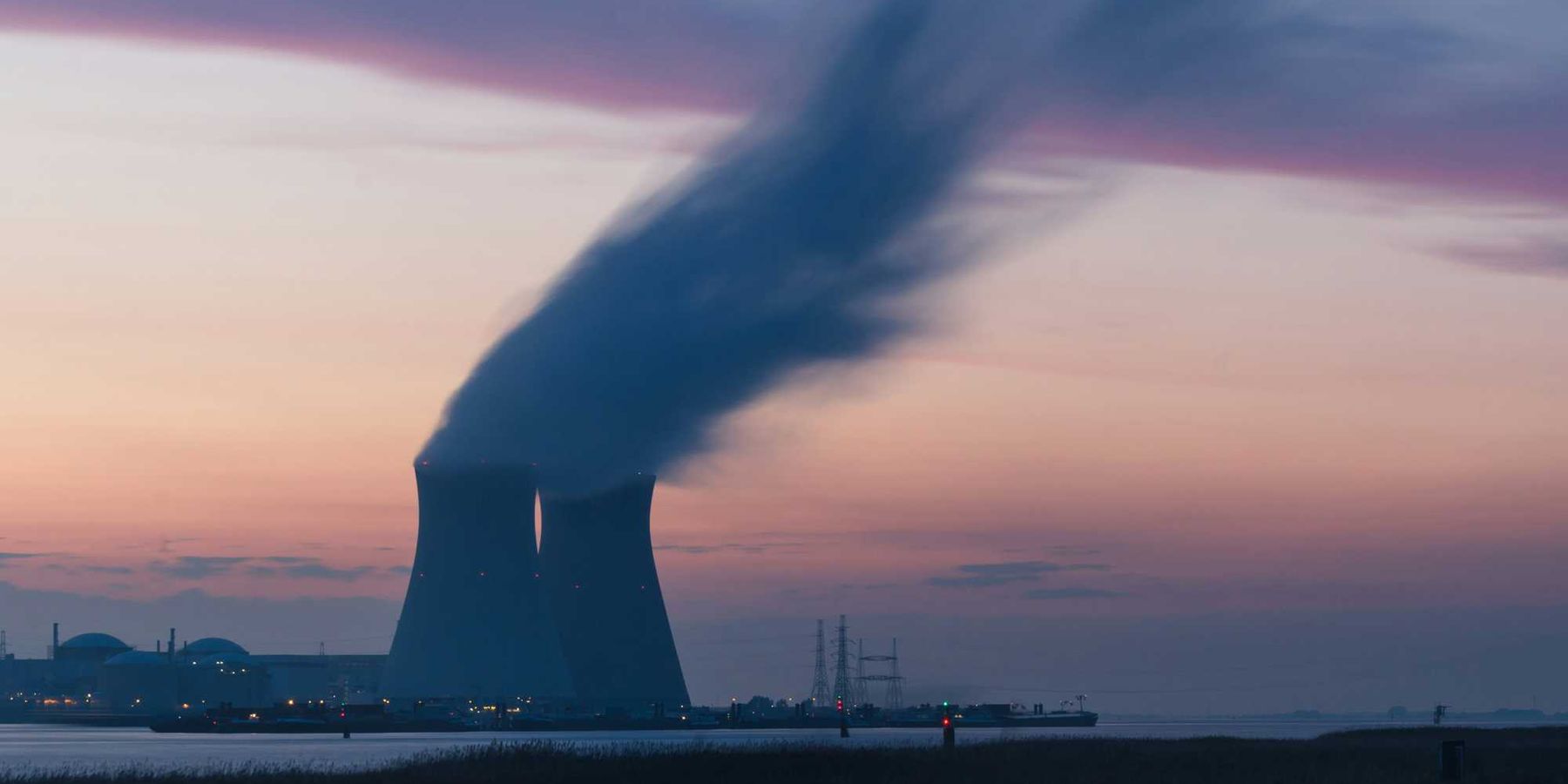 skyline photography of nuclear plant cooling tower blowing smokes under white and orange sky at daytime.