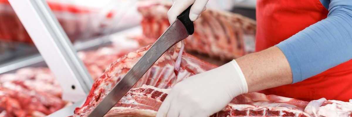 Slaughterhouse worker processing meat with a large knife