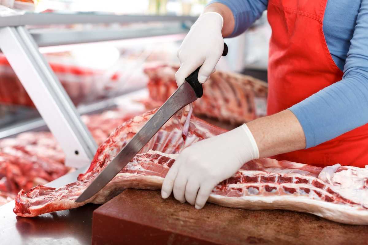 Slaughterhouse worker processing meat with a large knife