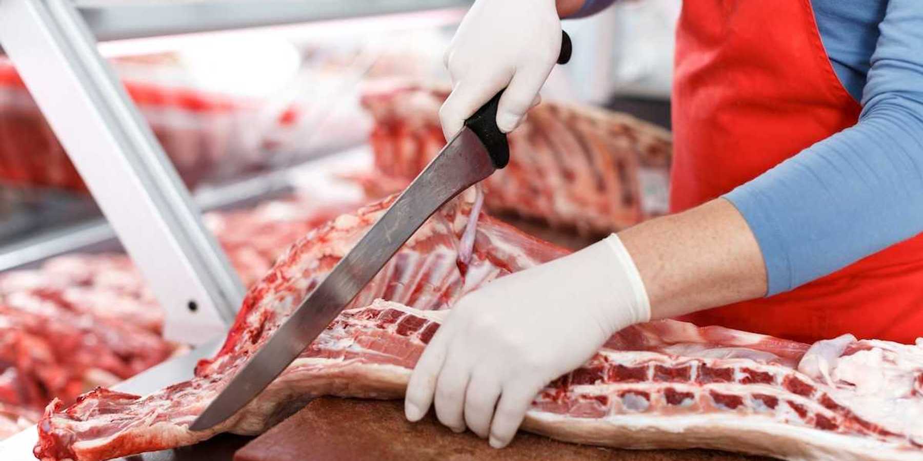 Slaughterhouse worker processing meat with a large knife