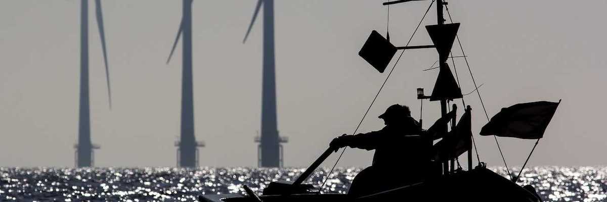 Small one-man fishing boat silhouetted at sunrise with sustainable energy wind turbines in the background.