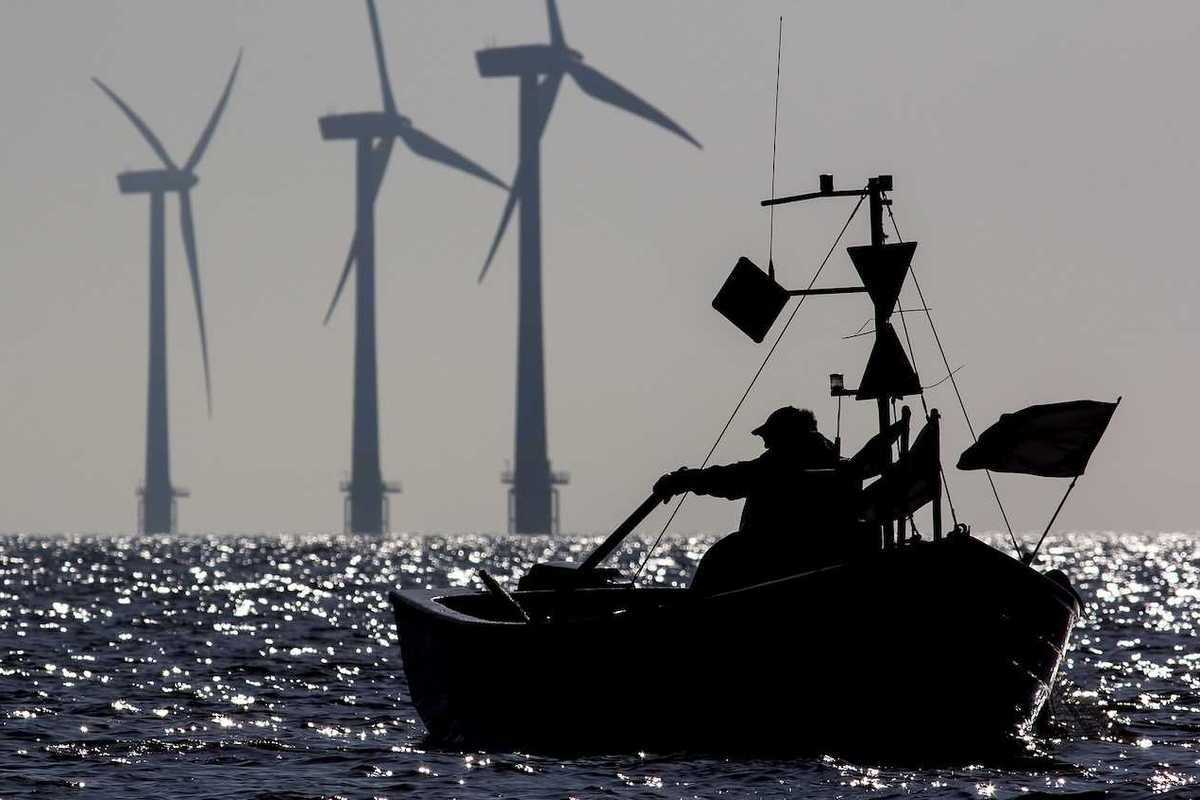 Small one-man fishing boat silhouetted at sunrise with sustainable energy wind turbines in the background.
