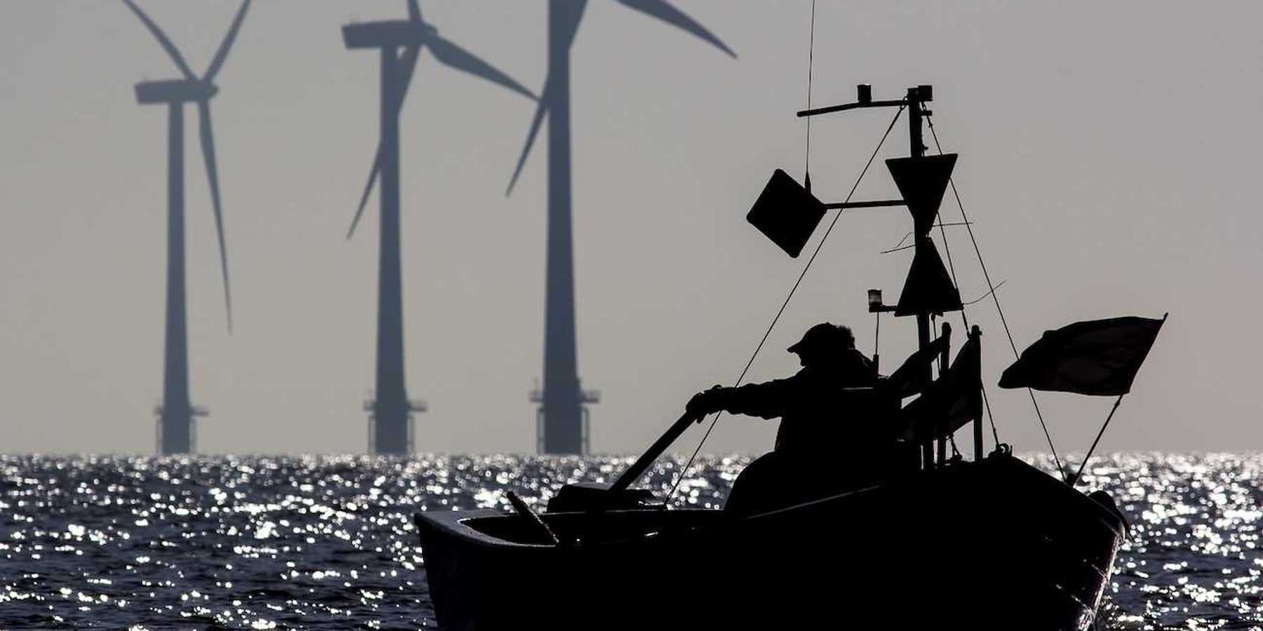 Small one-man fishing boat silhouetted at sunrise with sustainable energy wind turbines in the background.