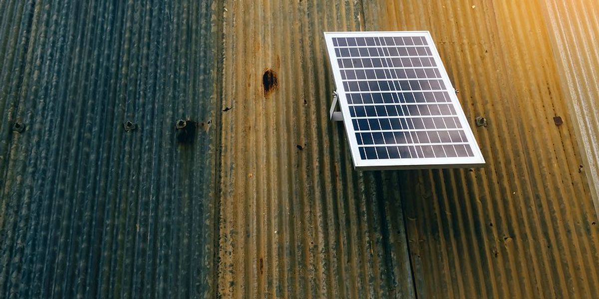 Small solar panel hanging on a rusted metal wall.