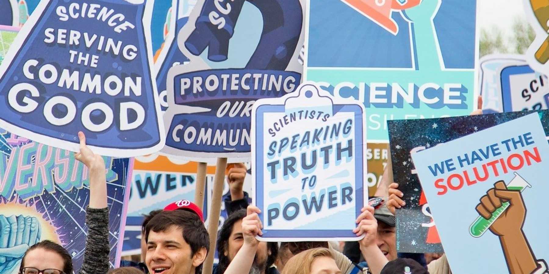 Smiling people with signs marching in support of science.