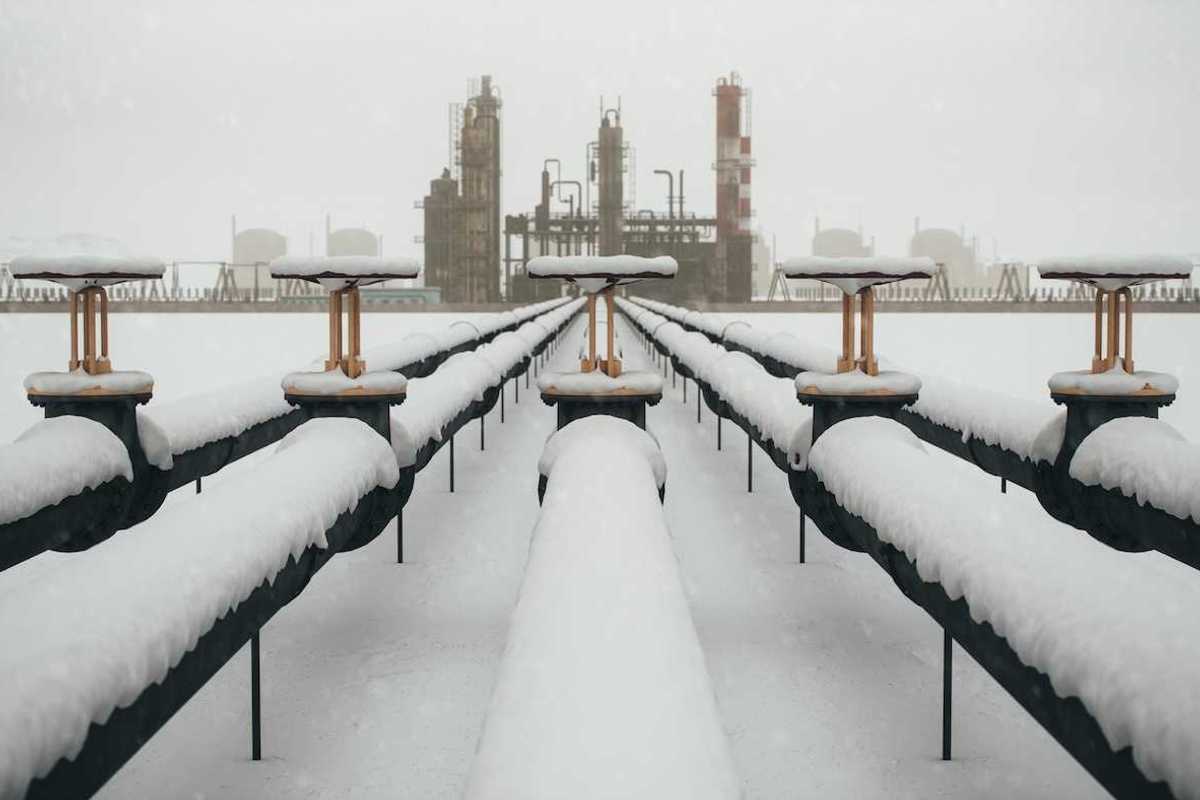 Snow-covered fossil fuel pipeline leading to a refinery.