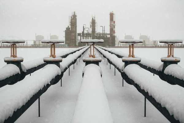 Snow-covered fossil fuel pipeline leading to a refinery.
