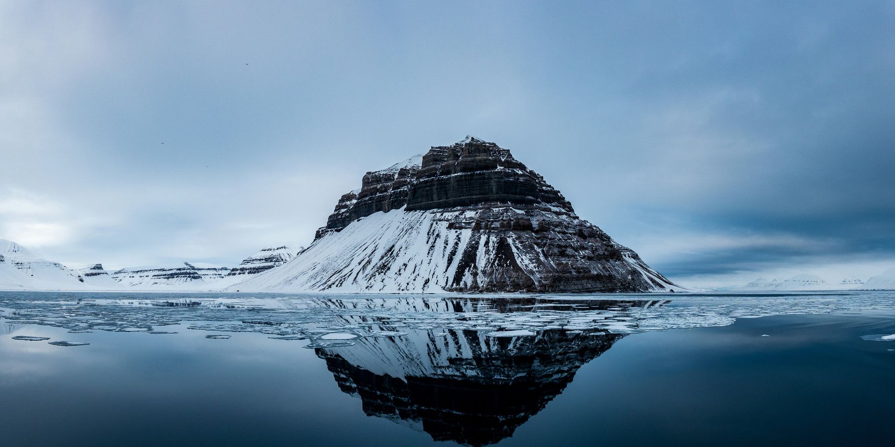 Snow covered mountain near body of water.