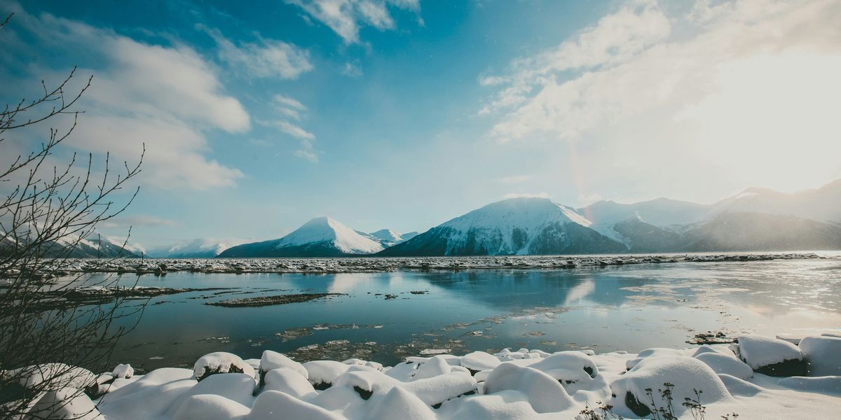Snow covered mountains in front of a body of water on a sunny day.