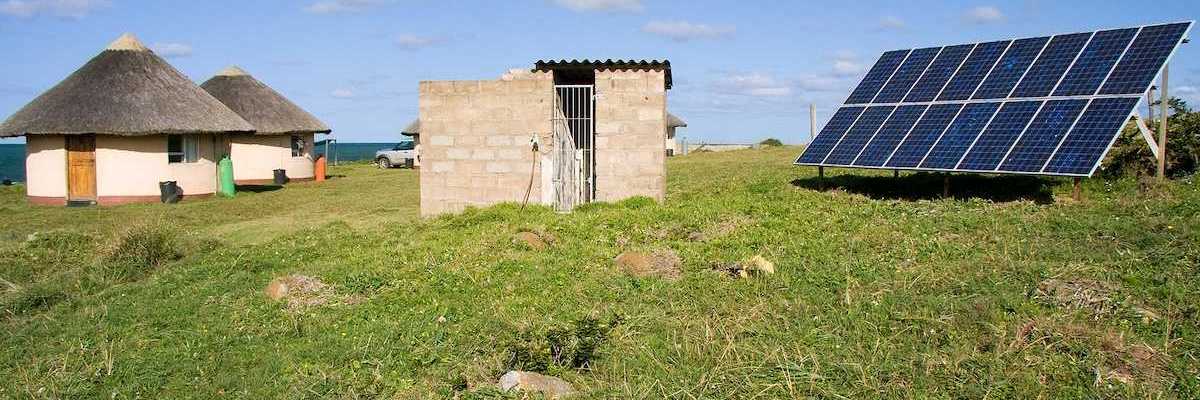 Solar panel providing power to a rural area in Africa. Detached array powering two thatched-roof buildings.