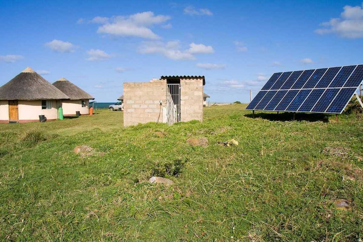Solar panel providing power to a rural area in Africa. Detached array powering two thatched-roof buildings.