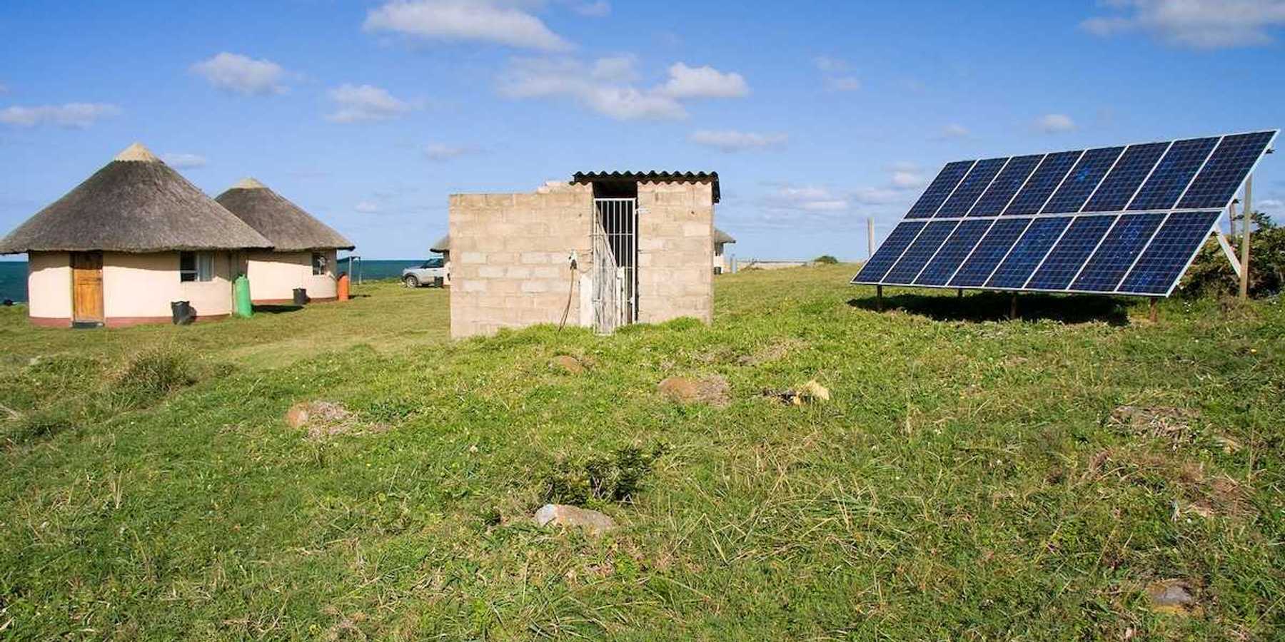 Solar panel providing power to a rural area in Africa. Detached array powering two thatched-roof buildings.
