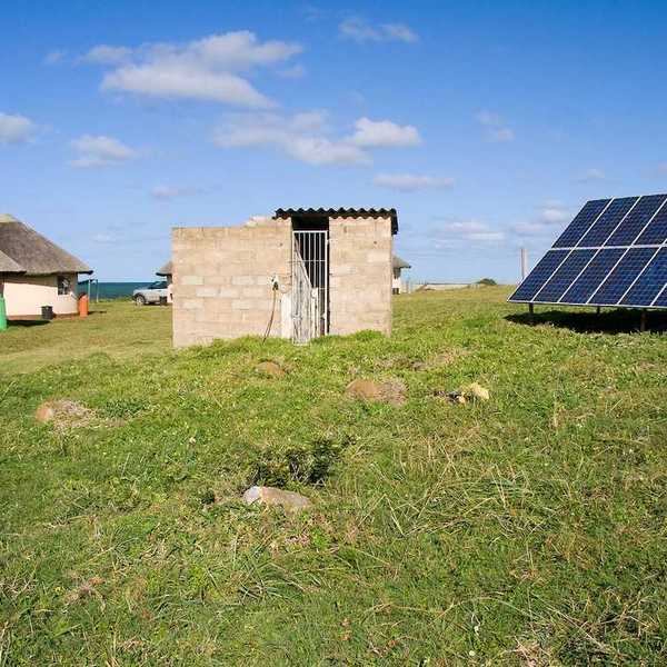 Solar panel providing power to a rural area in Africa. Detached array powering two thatched-roof buildings.