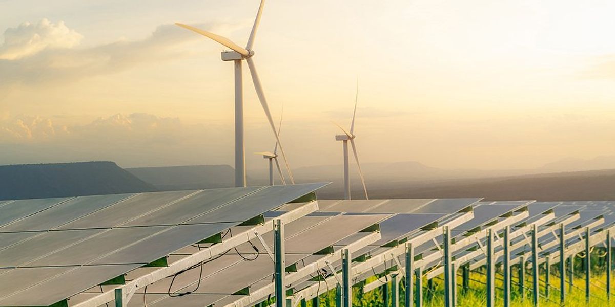 Solar panels and wind turbones in a grassy field with mountains in background.