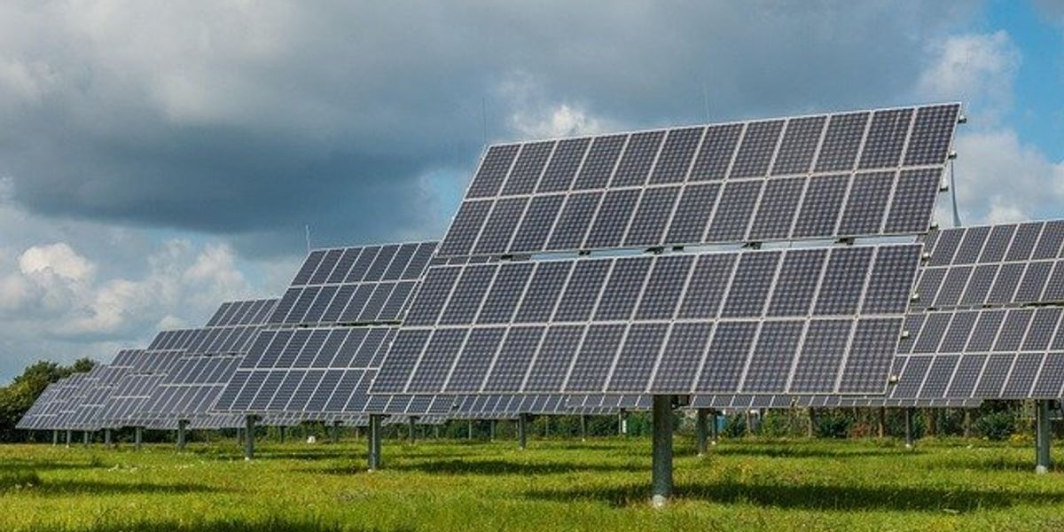 Solar panels in a green field under partly cloudy skies.