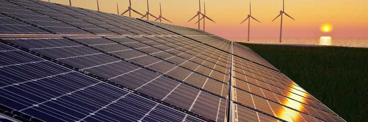 Solar panels in foreground with wind turbines and a setting (or rising) sun in background
