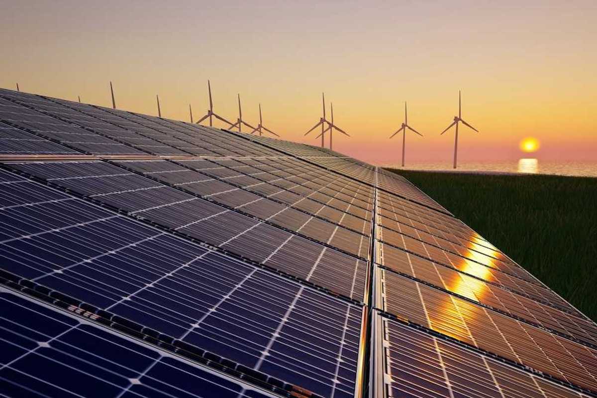 Solar panels in foreground with wind turbines and a setting (or rising) sun in background