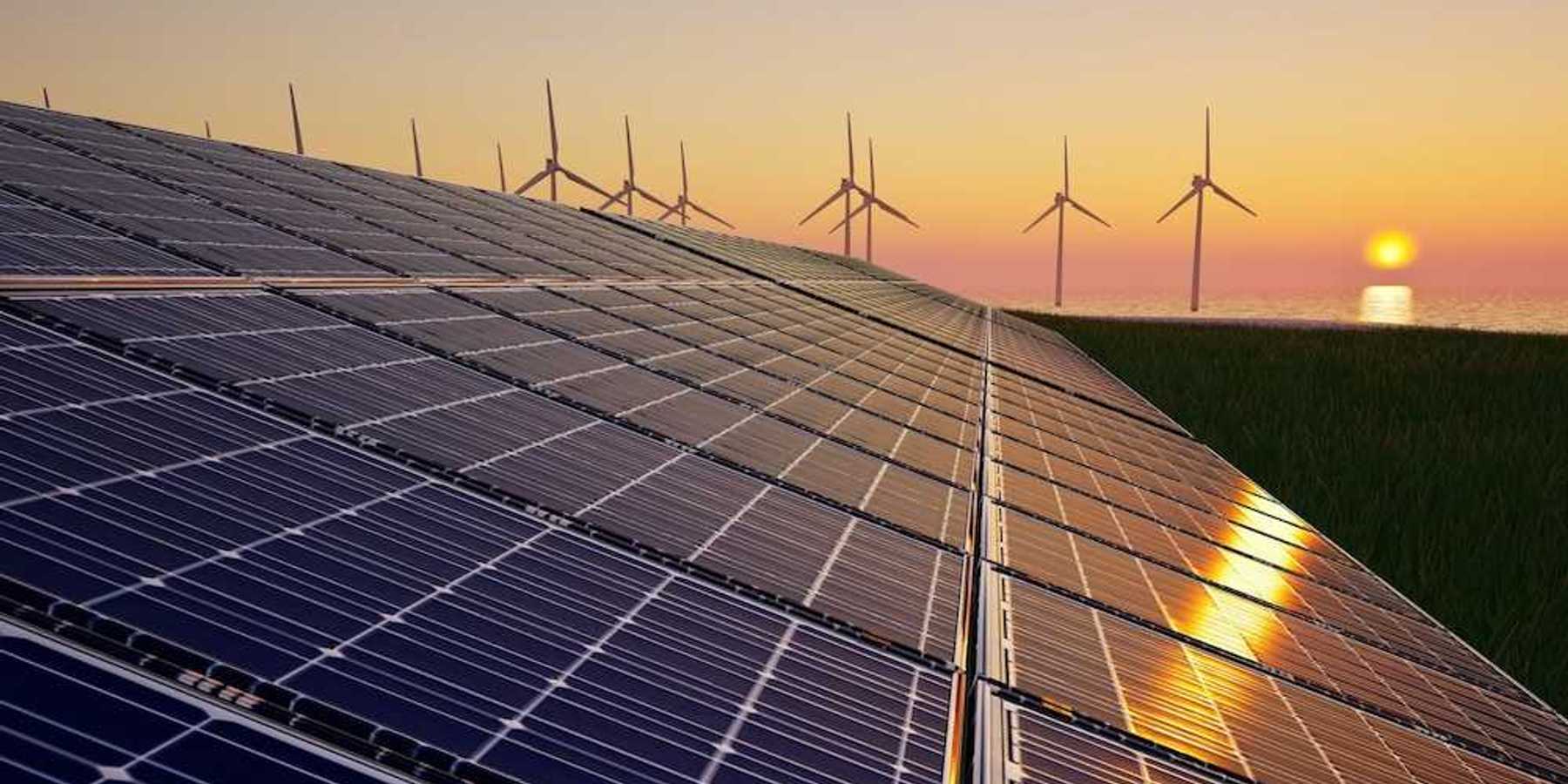 Solar panels in foreground with wind turbines and a setting (or rising) sun in background