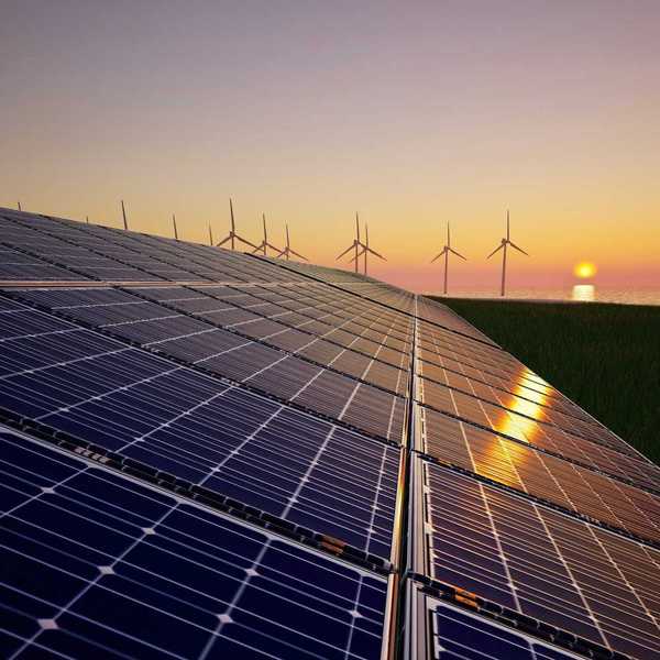 Solar panels in foreground with wind turbines and a setting (or rising) sun in background