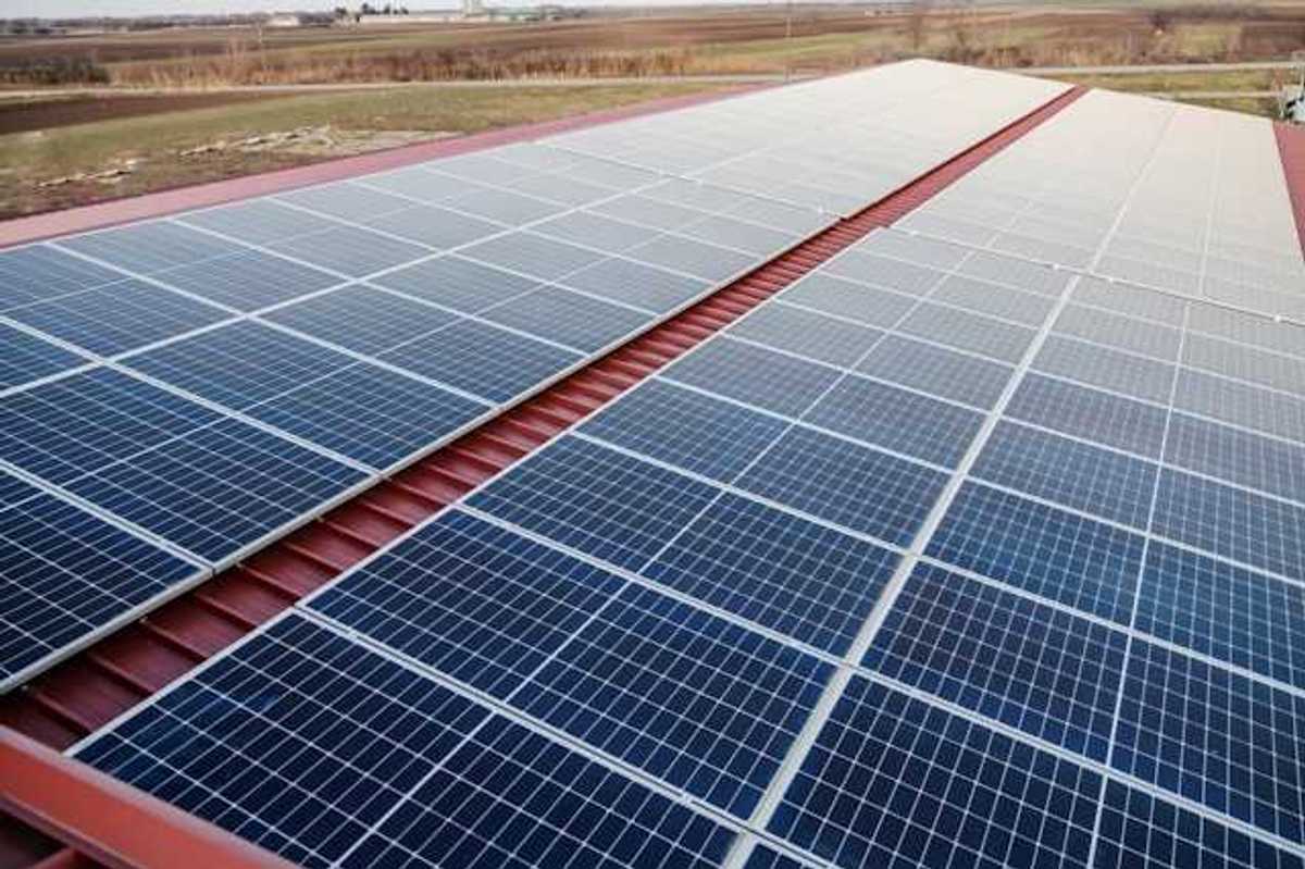 Solar panels on a red metal roof with a green landscape in the background