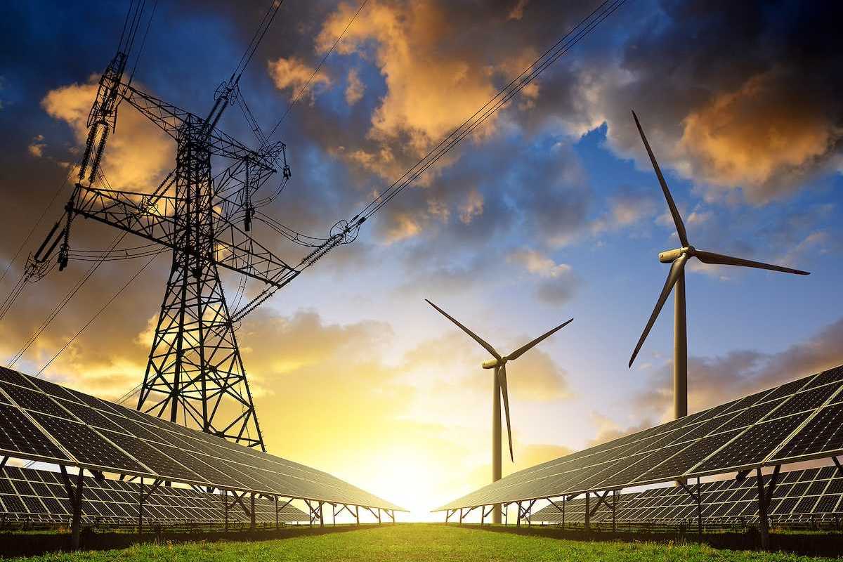 Solar panels with wind turbines beneath electrical transmission lines at sunset.