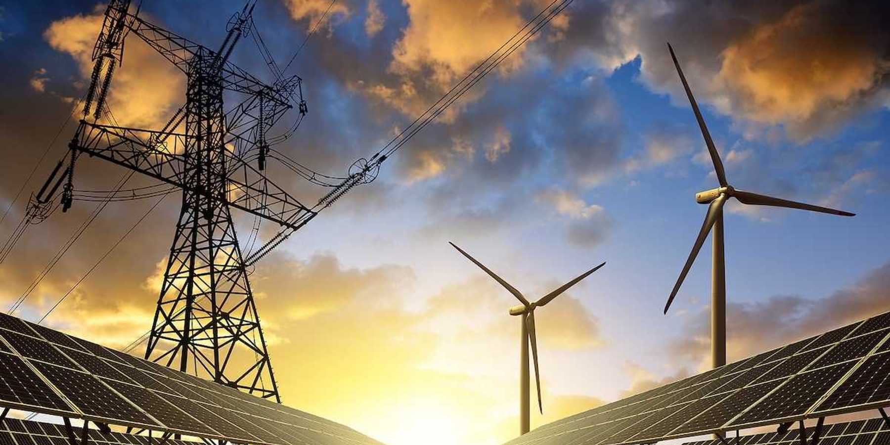 Solar panels with wind turbines beneath electrical transmission lines at sunset.