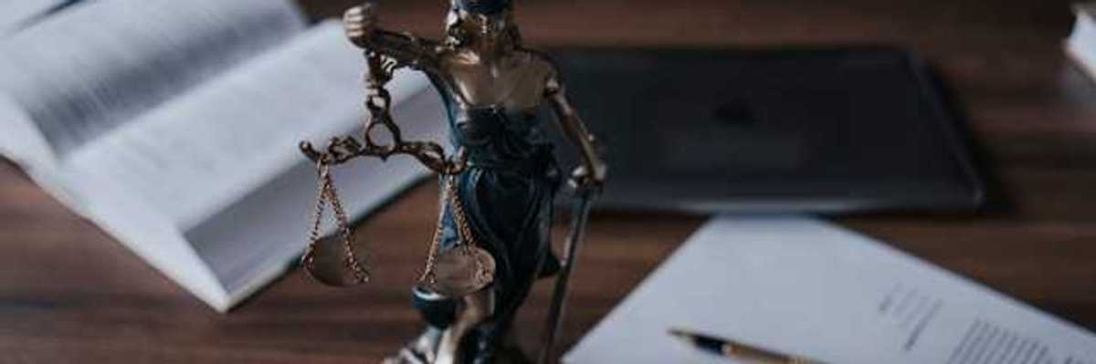 Statue of lady justice on a wooden desk with legal manuals and documents nearby