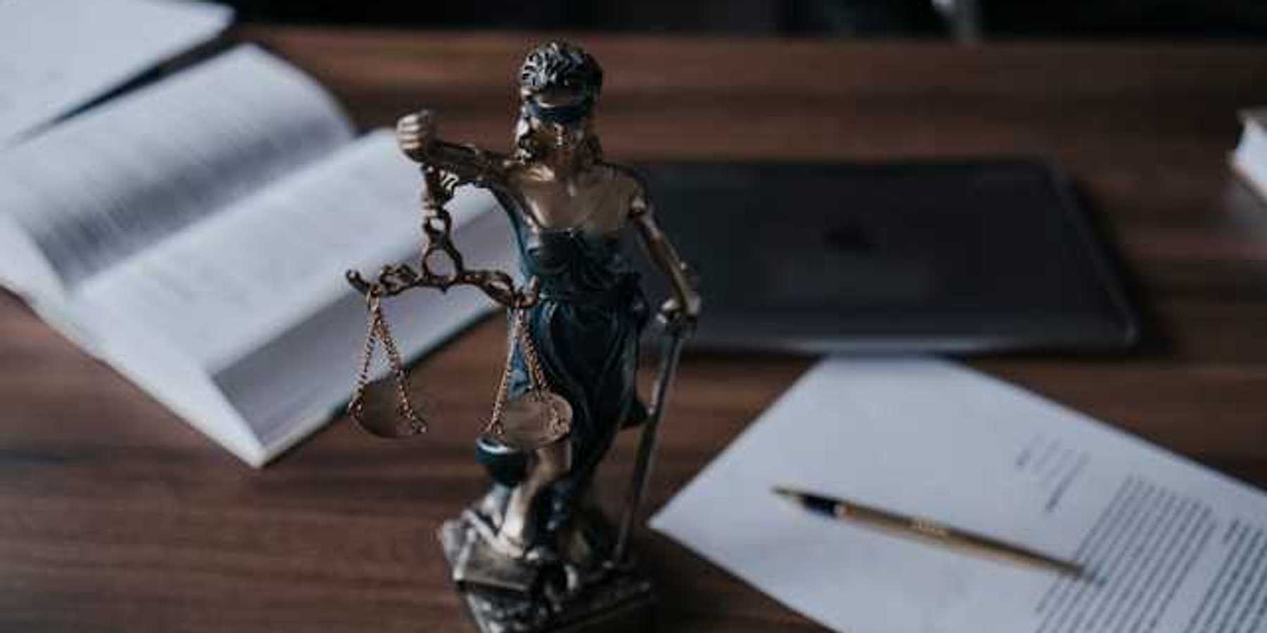 Statue of lady justice on a wooden desk with legal manuals and documents nearby