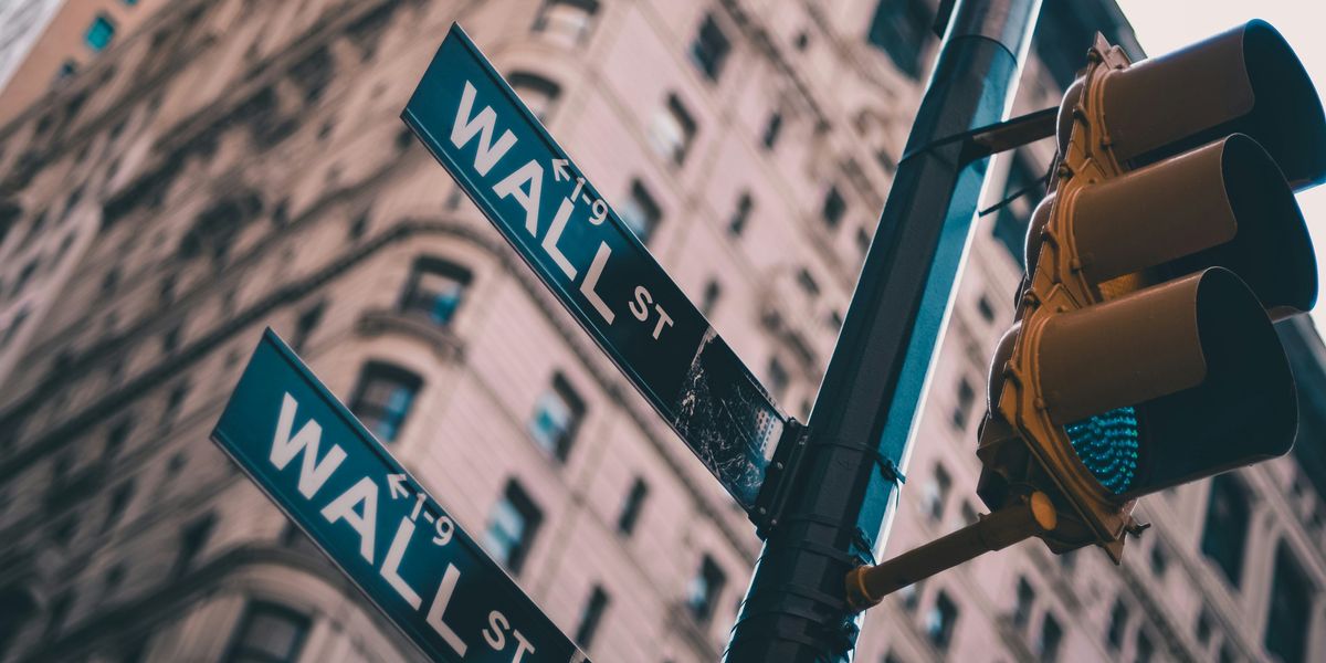 Street signs saying Wall St with a skyscraper in the background.