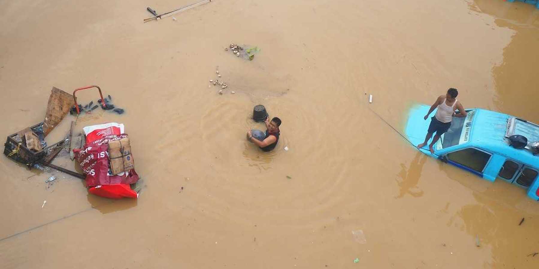 Submerged street in Jakarta, Indonesia with two blue vehicles submerged to their windows - one with a man on the hood.
