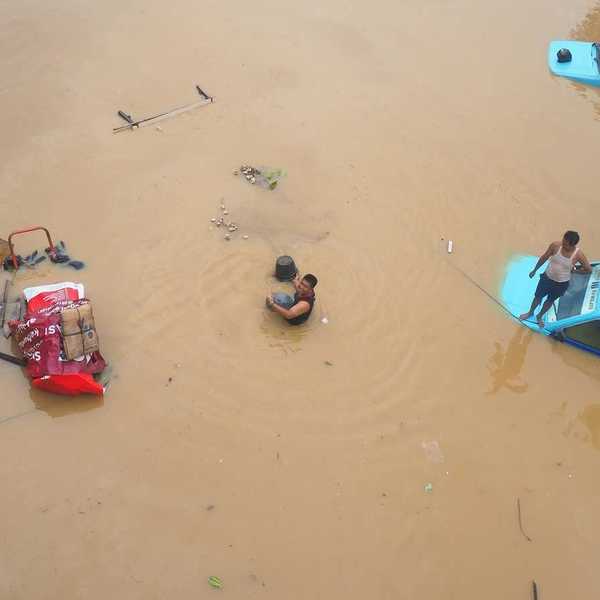 Submerged street in Jakarta, Indonesia with two blue vehicles submerged to their windows - one with a man on the hood.