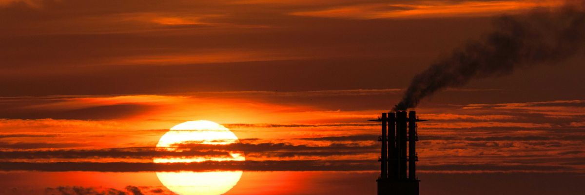 Sun setting behind a power plant smoke stack emitting pollution