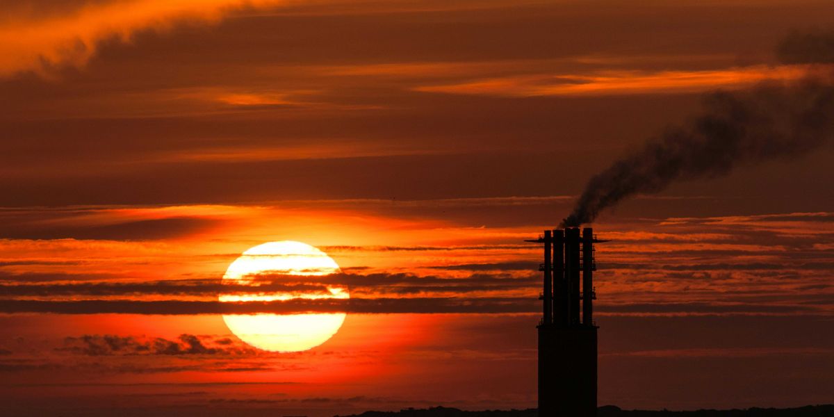 Sun setting behind a power plant smoke stack emitting pollution