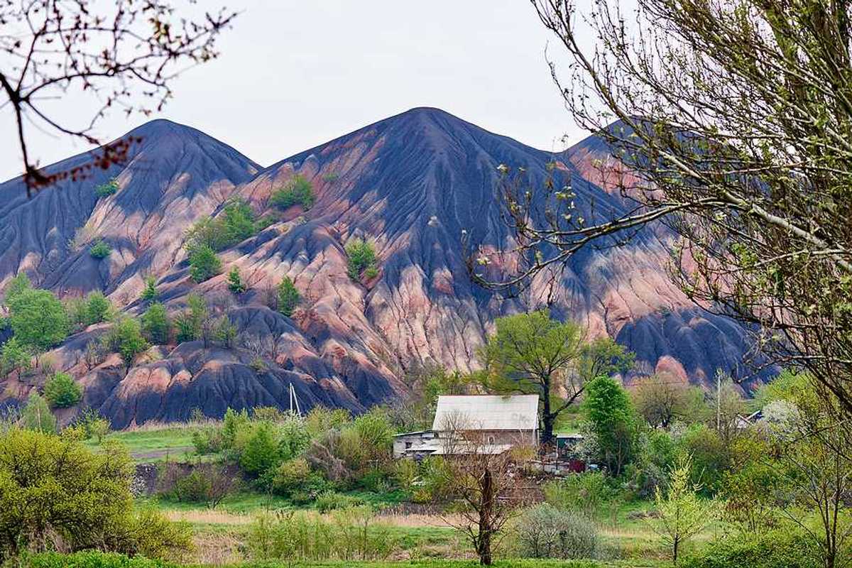 Tall slag heaps in the distance with green fields and trees in the foreground