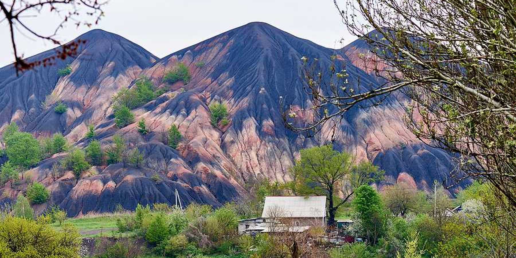 Tall slag heaps in the distance with green fields and trees in the foreground