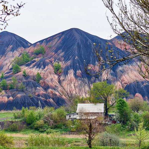 Tall slag heaps in the distance with green fields and trees in the foreground