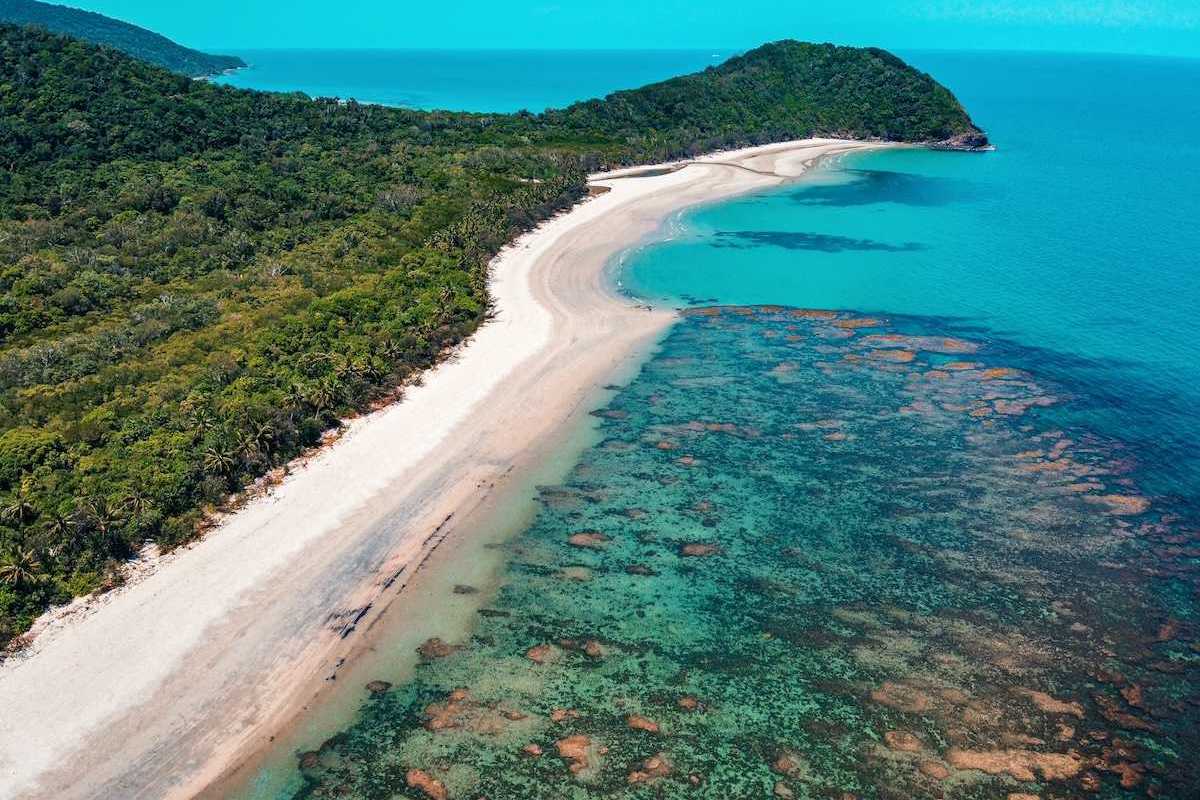 The Great Barrier Reef from above. Underwater, but visible, reef formation, with azure blue water and sky and land extendinginto ocean.