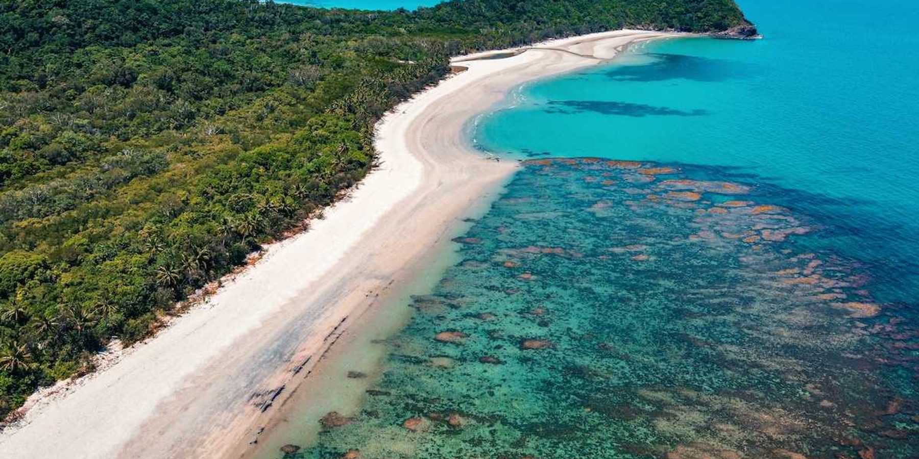 The Great Barrier Reef from above. Underwater, but visible, reef formation, with azure blue water and sky and land extendinginto ocean.