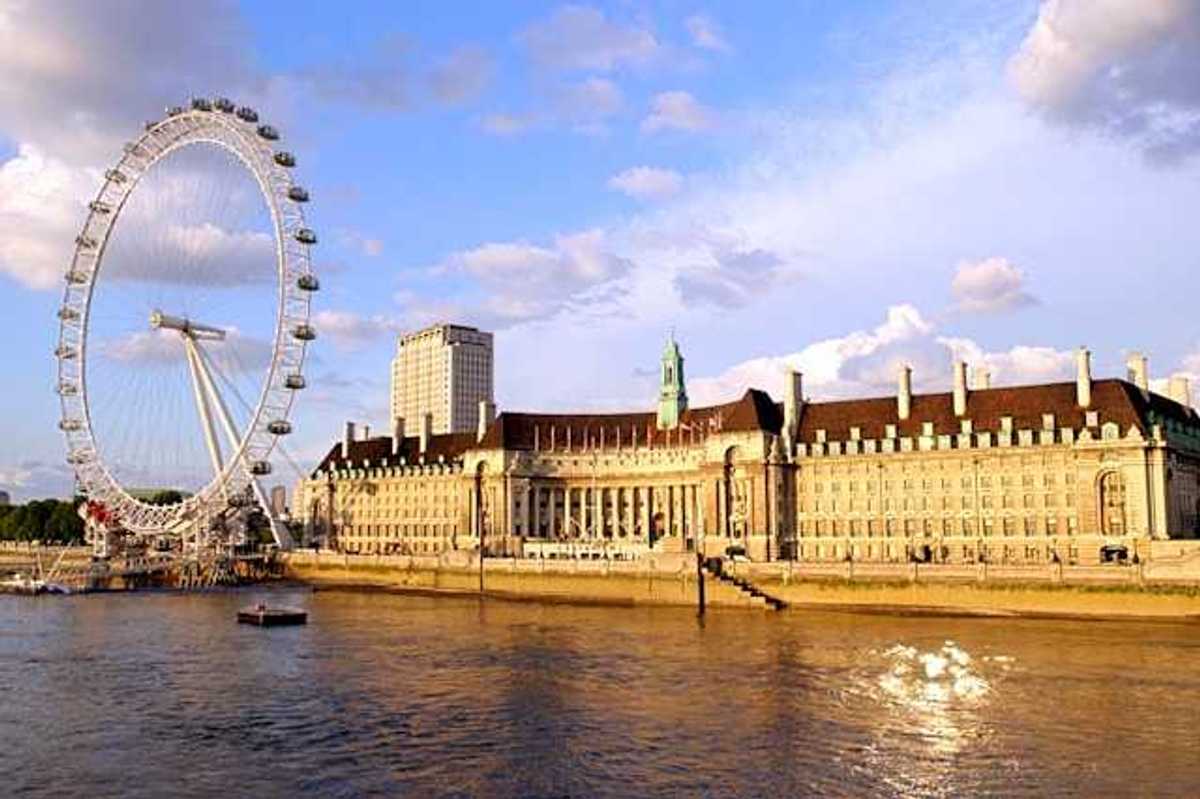 The River Thames and ferris wheel next to a large building on a sunny day