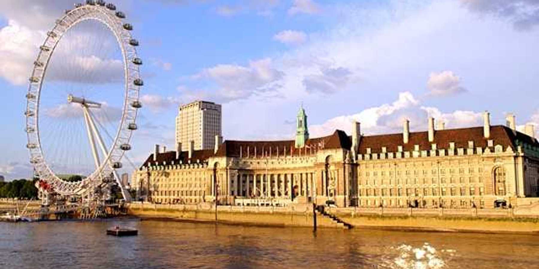 The River Thames and ferris wheel next to a large building on a sunny day