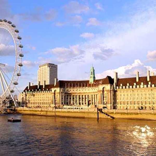 The River Thames and ferris wheel next to a large building on a sunny day