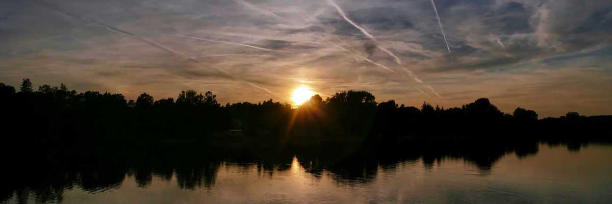 the sun is setting over a lake with contrails in the sky