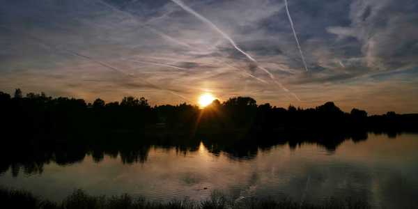 the sun is setting over a lake with contrails in the sky