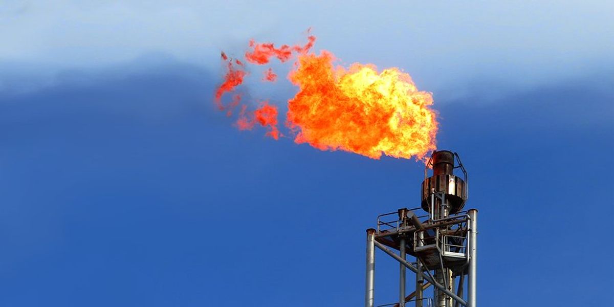 The top of a gas tower flaring with flames shooting out the top.