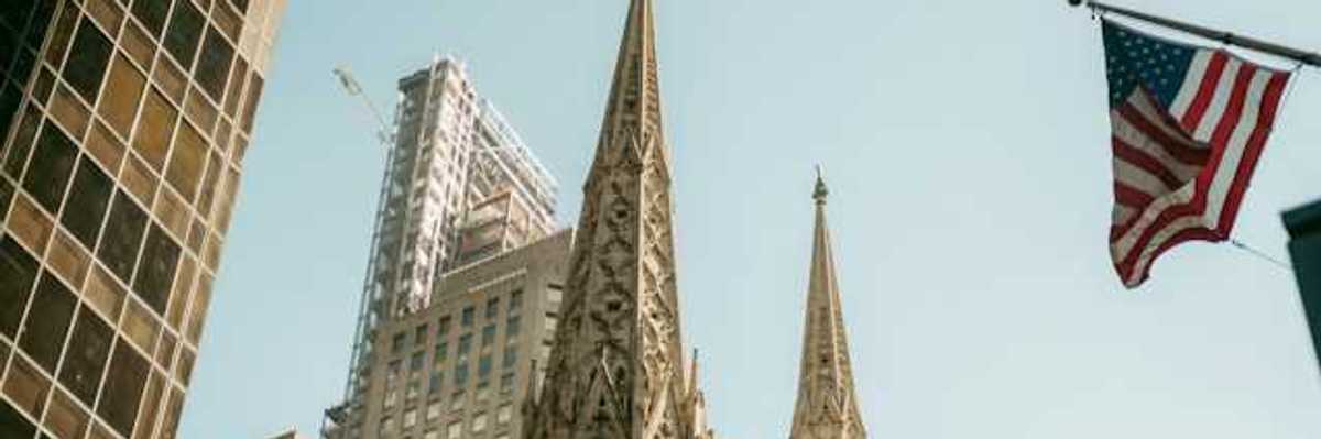 The top portion of a cathedral in a city with buildings surrounding it