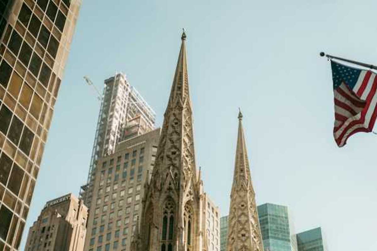 The top portion of a cathedral in a city with buildings surrounding it