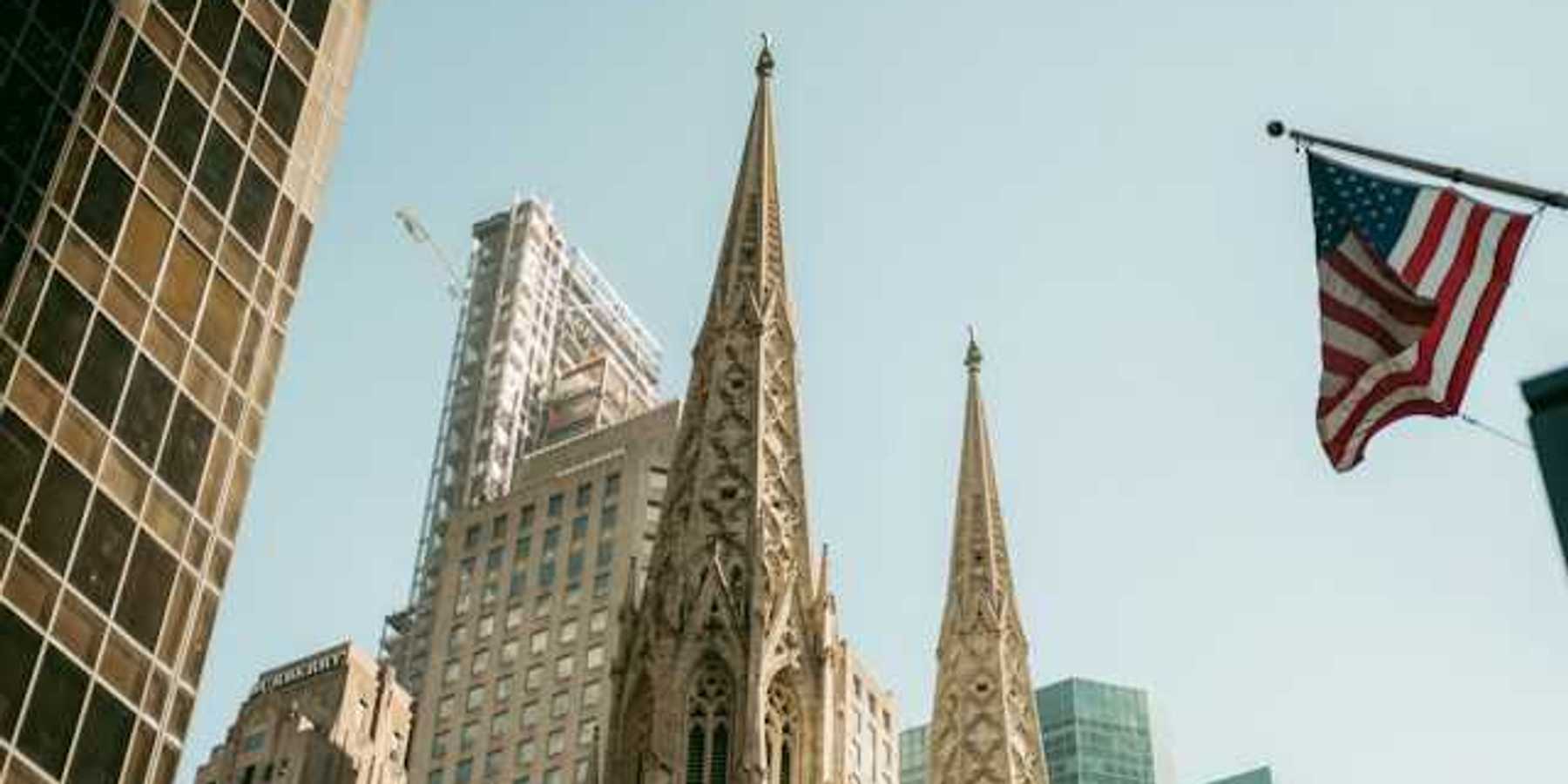 The top portion of a cathedral in a city with buildings surrounding it